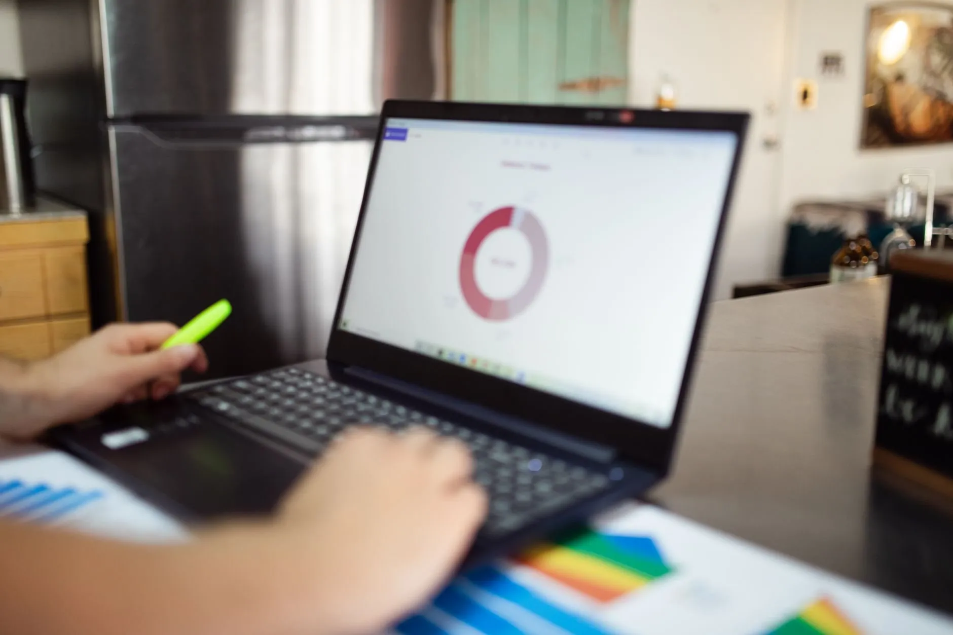 A hand holding a highlighter beside a laptop showing a donut chart